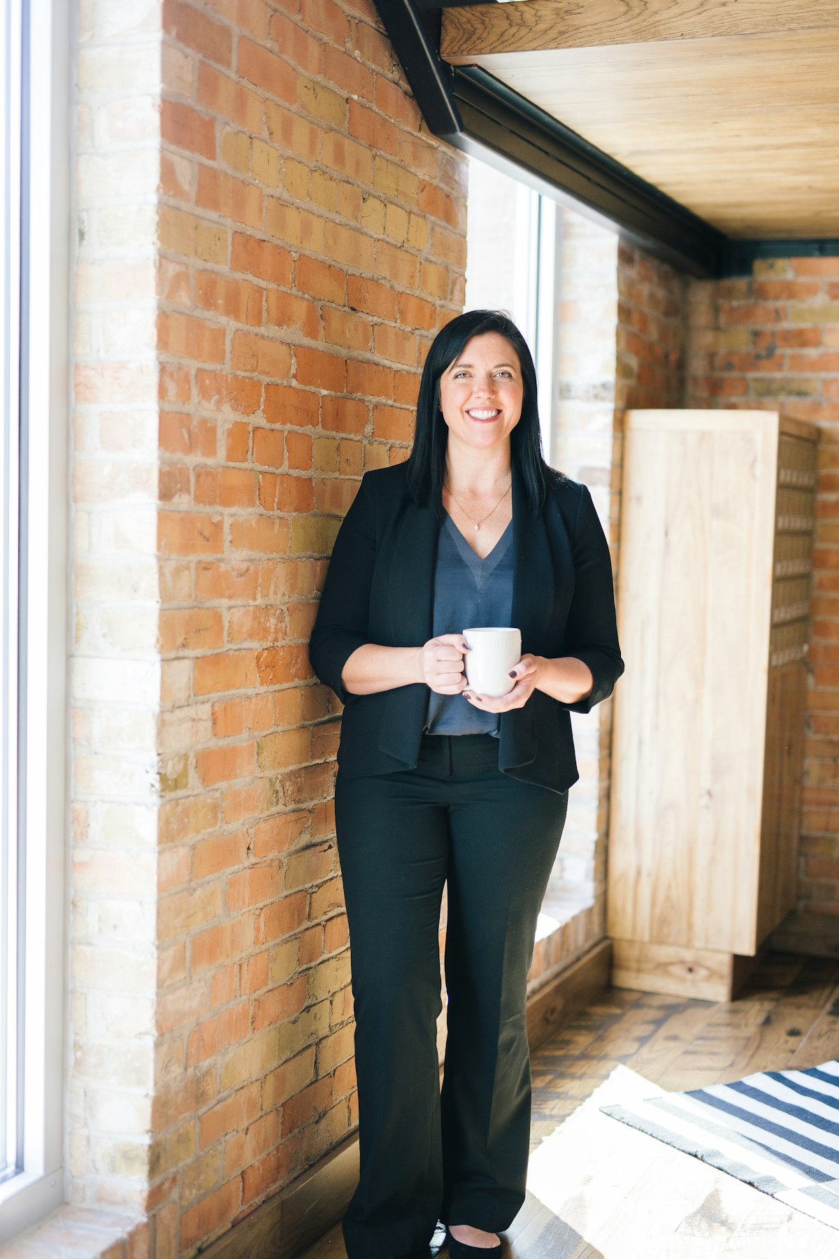 A financial planner standing in a bright office, holding a mug, ready to meet a family.